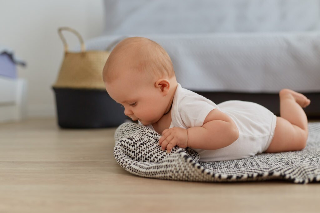 portrait pretty crawling baby girl posing indoor floor studying world around small kid wearing white bodysuit lying grey carpet near sofa